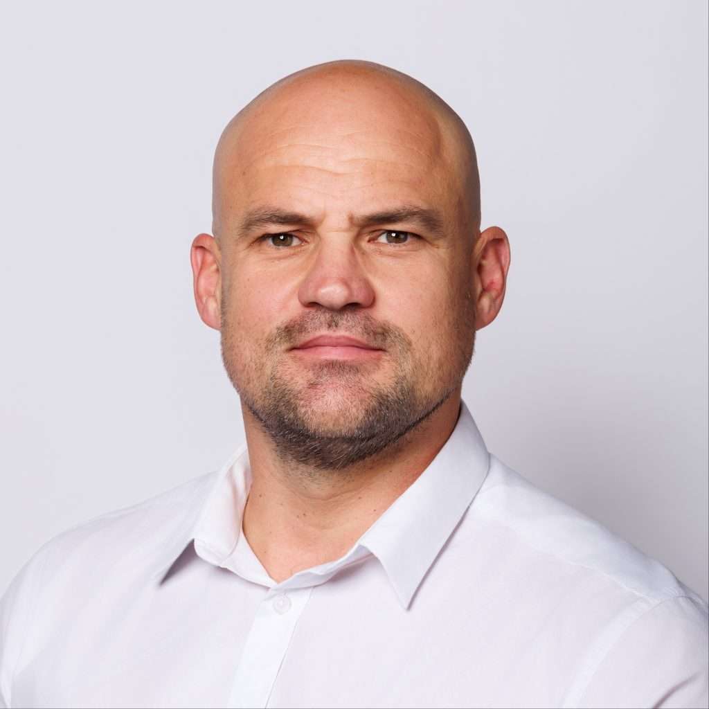 Close-up portrait of a bald man in a white shirt facing forward.